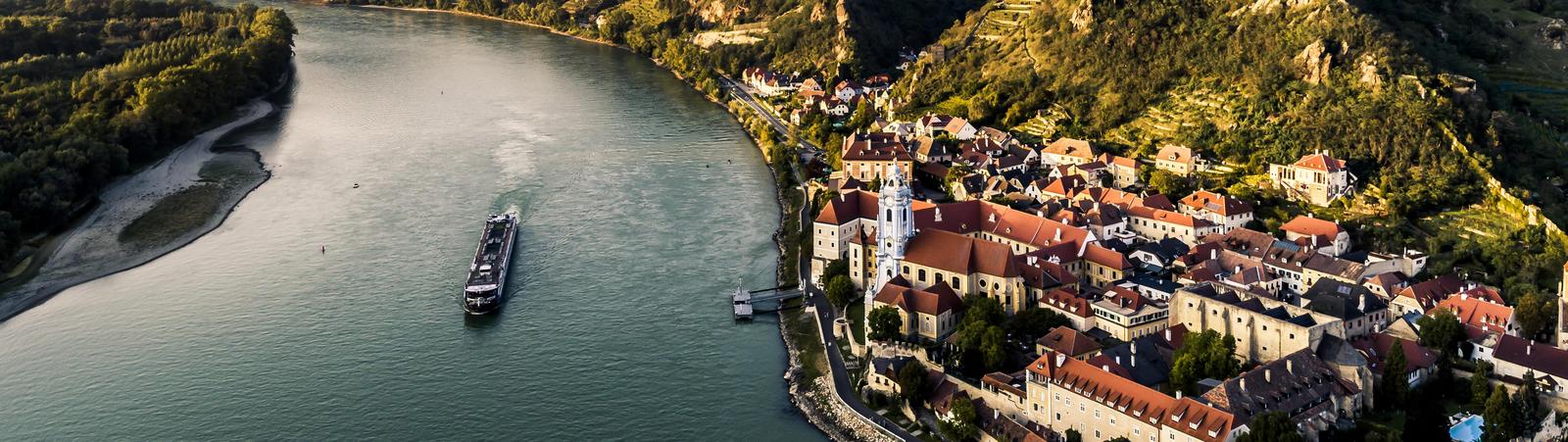 Blick über den Fluss Donau mit Boot und das Tal Wachau mit dem Dorf Dürnstein im Vordergrund